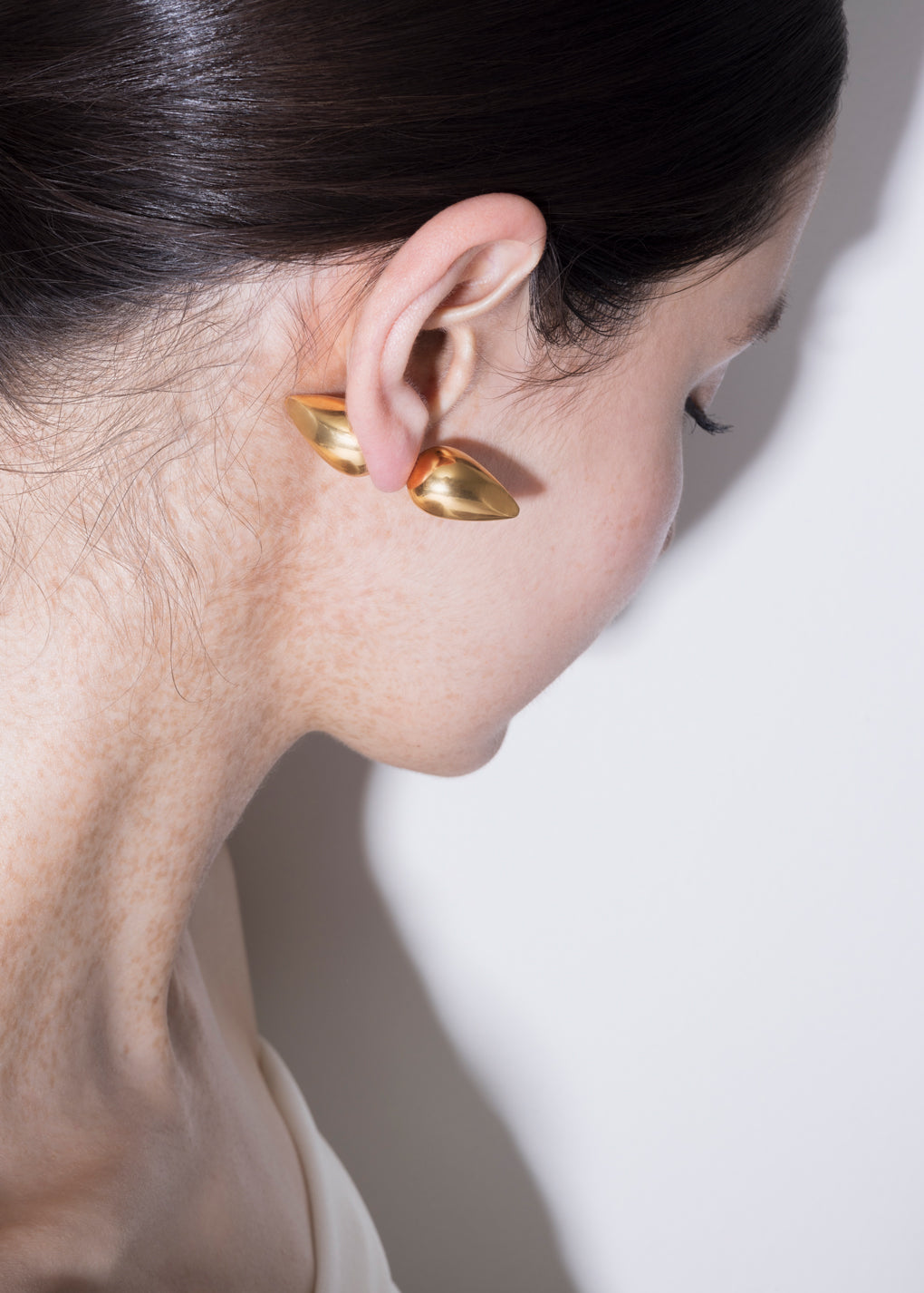 Close-up of a woman wearing gold plated vintage piercing earrings with a sleek design.