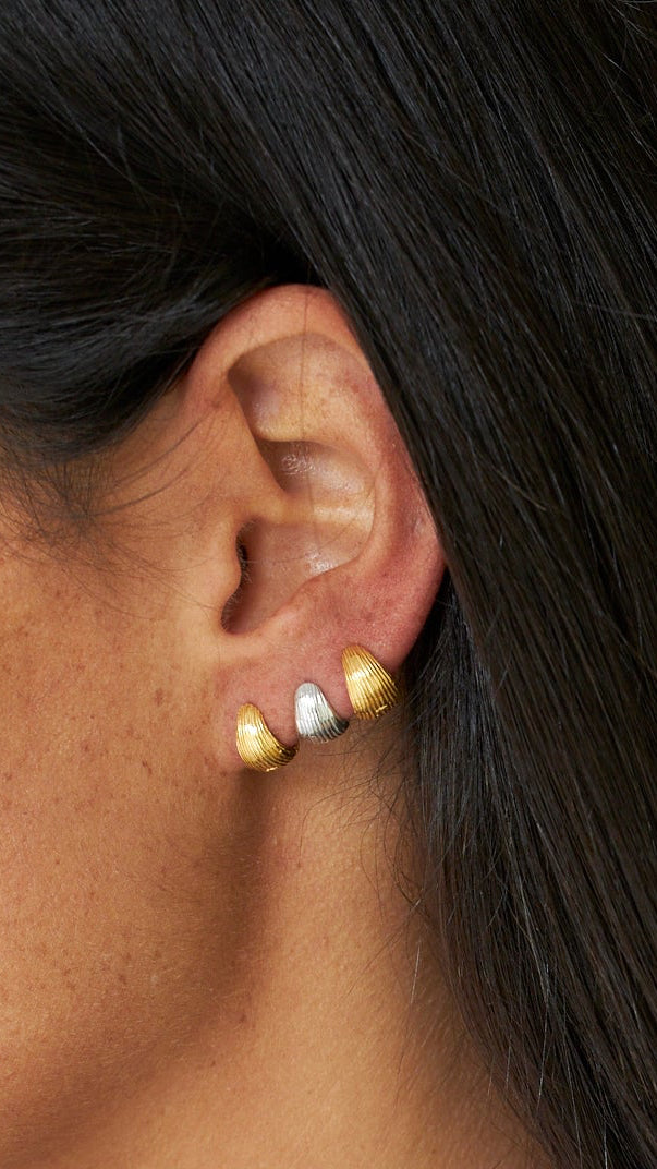 Close-up of an ear wearing gold earrings with a neutral background