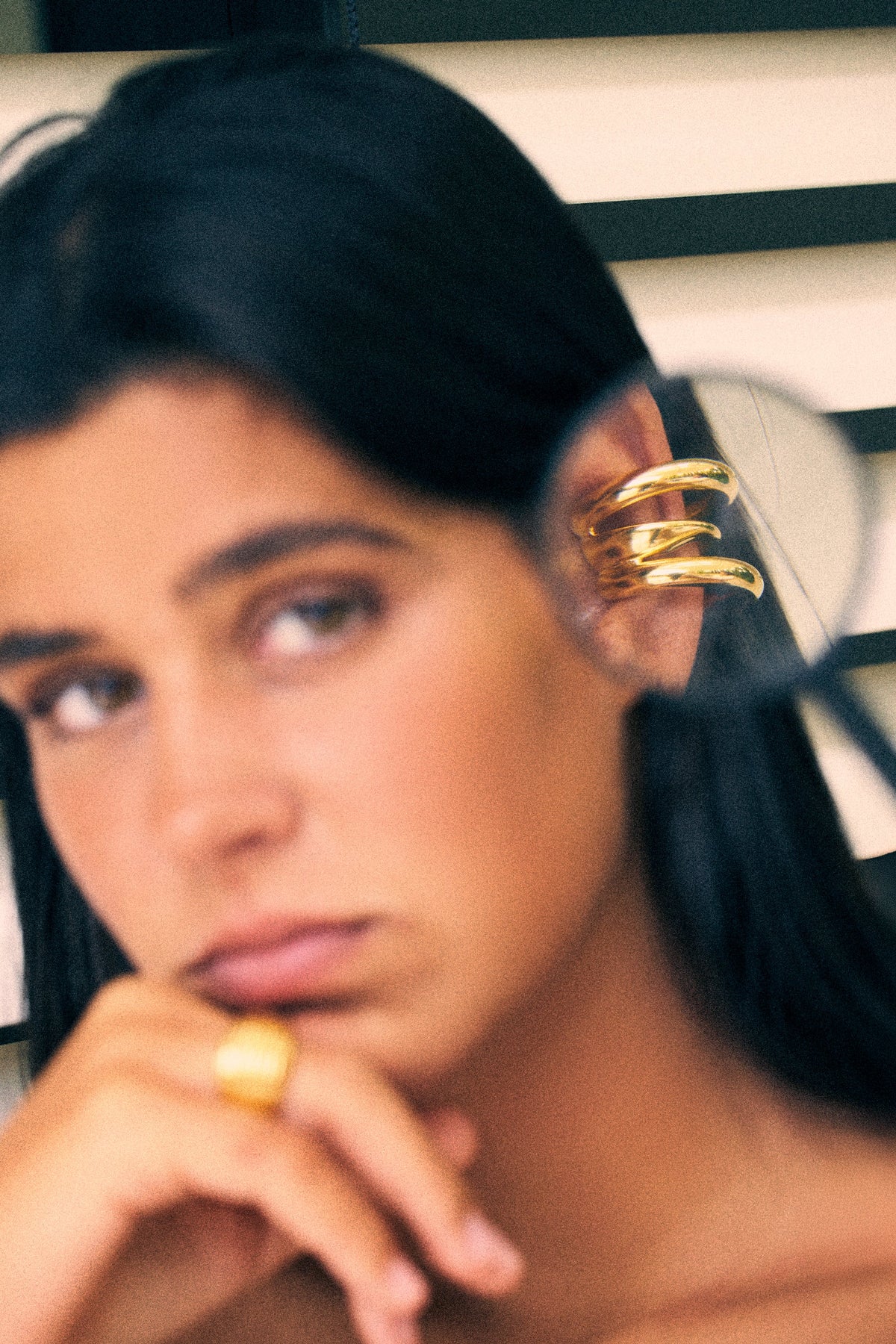 Gold no piercing ear cuffs worn on the ear of a model, with a soft focus on the face.