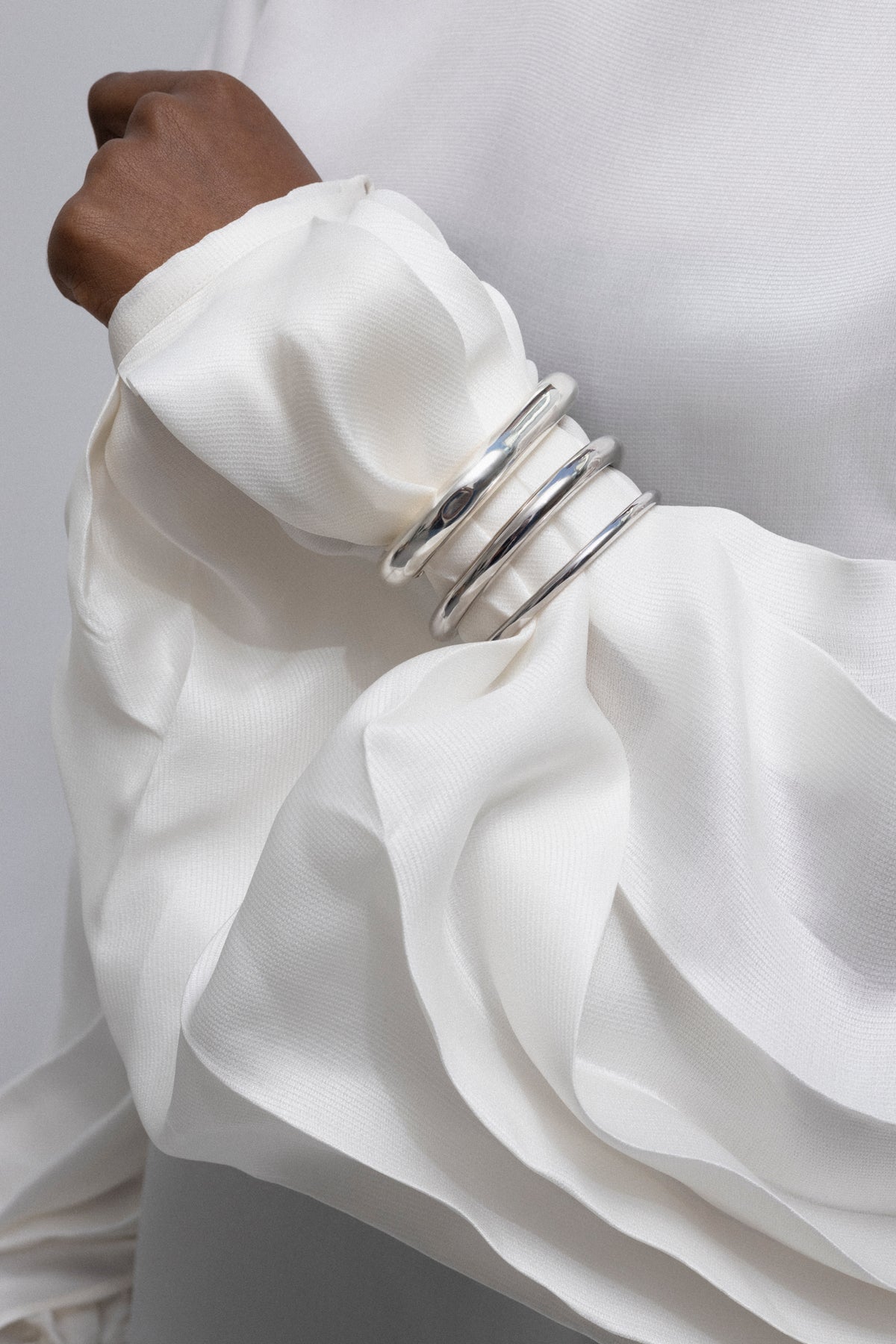Close-up of a wrist adorned with multiple statement cuff bangles in silver, showcasing elegance and structure.