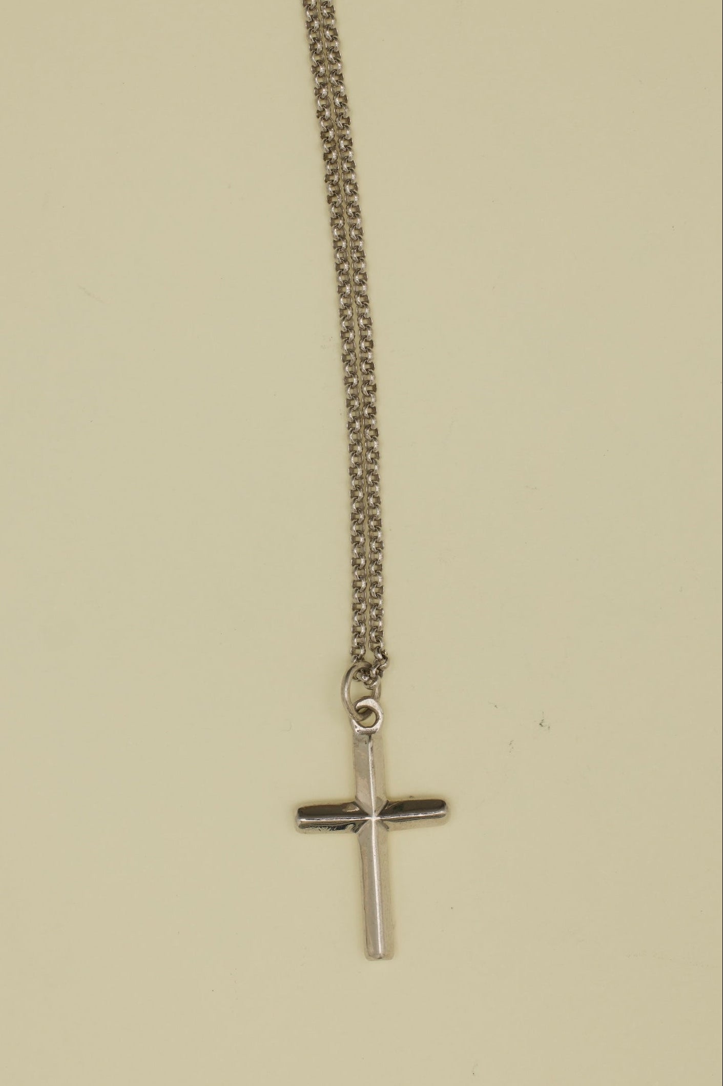 Silver chain necklace with a cross pendant on a beige background
