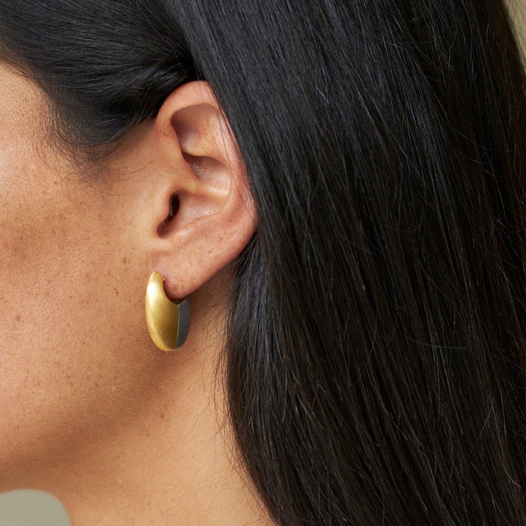 Close-up of a person wearing gold hoop earrings with a neutral background
