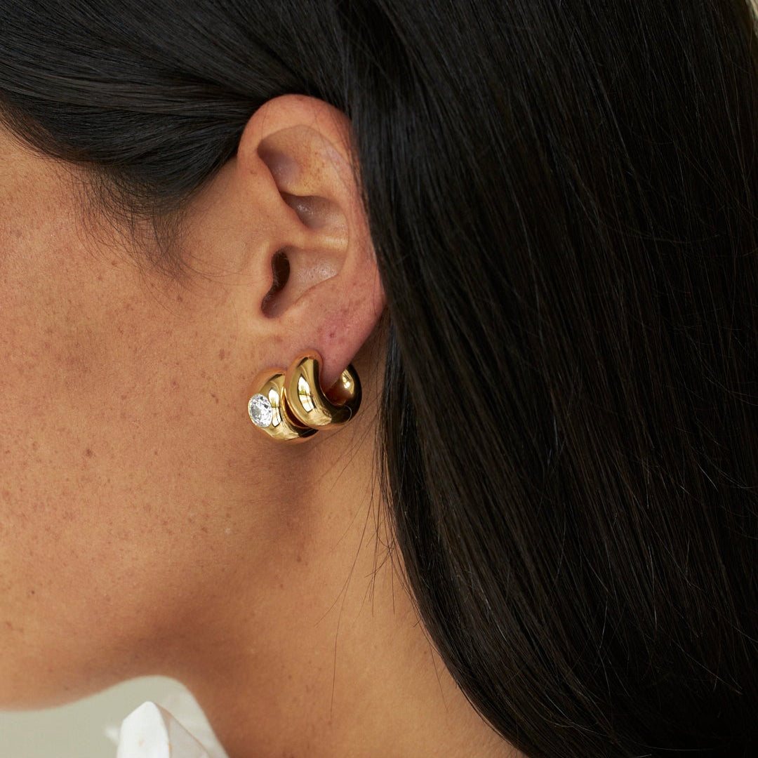 Close-up of a person wearing gold hoop earrings with a white blouse.
