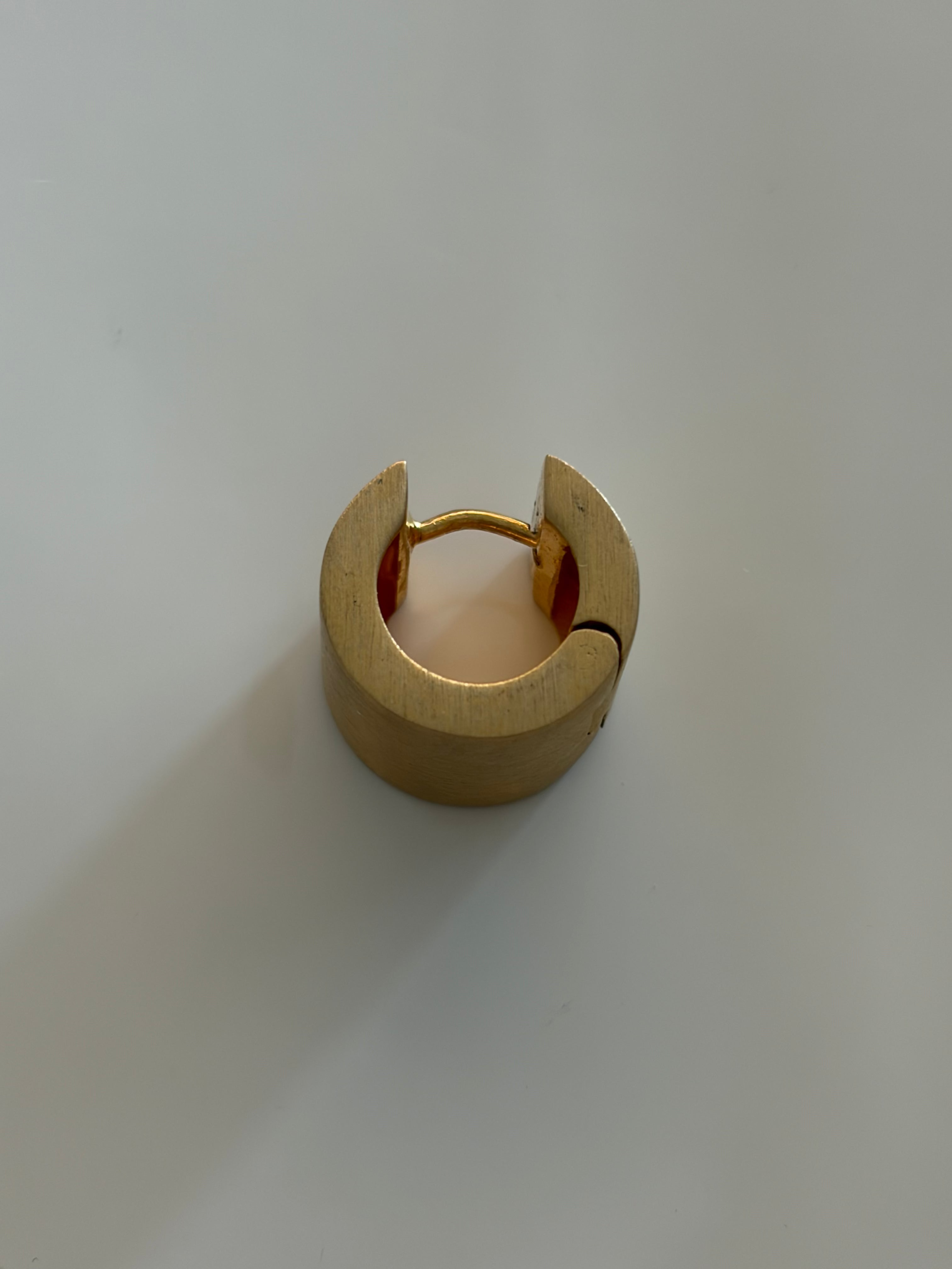A gold-colored metal ring with a split circular design and a small inner gold loop, photographed on a plain light background.
