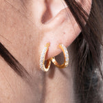 Close-up of a person wearing gold hoop earrings with embedded stones.