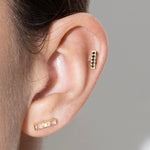 Close-up of an ear wearing gold earrings against a neutral background