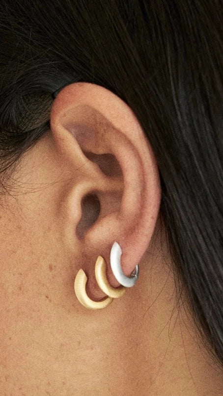 Close-up of a person wearing gold hoop earrings with a blurred background