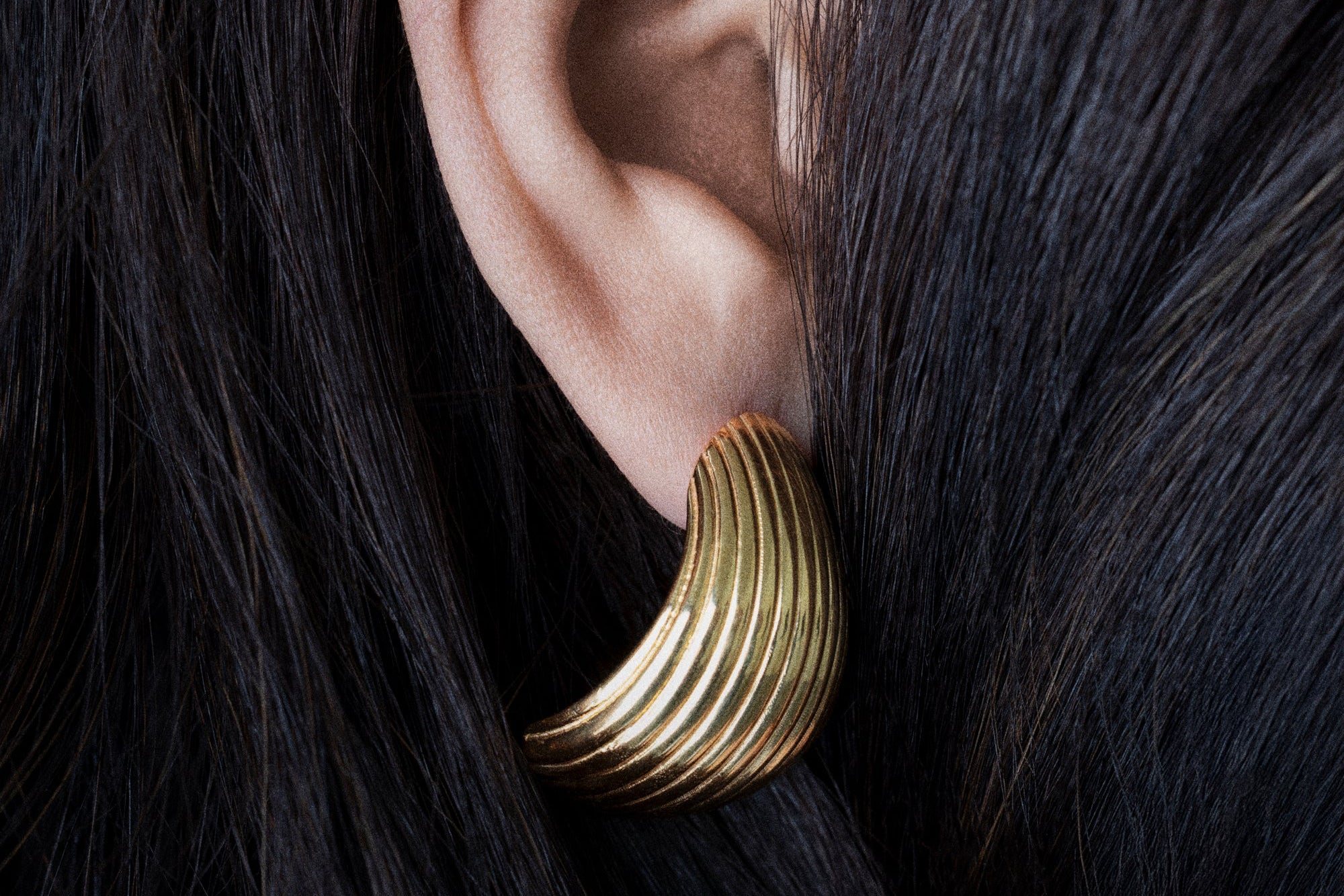 Gold earring worn by a person with dark hair on a black background