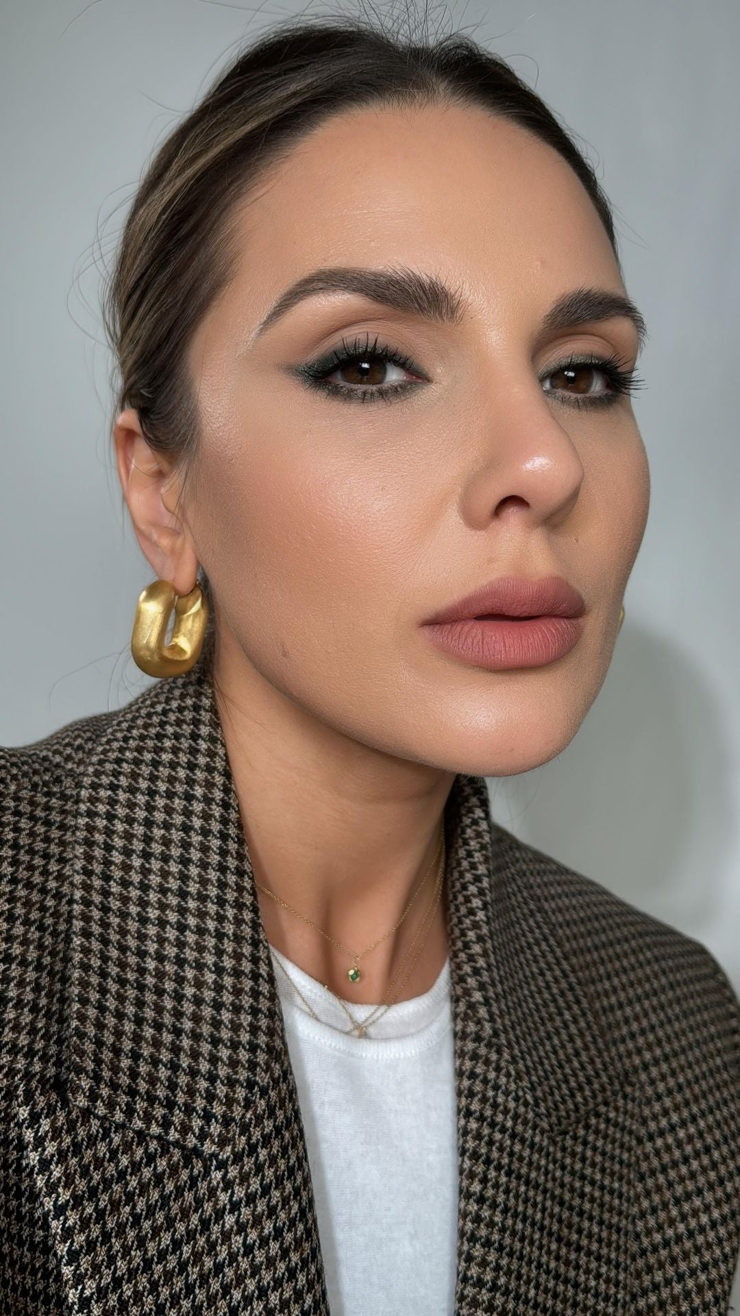 CINCO gold earrings worn on ear, enhancing a sophisticated look with makeup and patterned blazer.