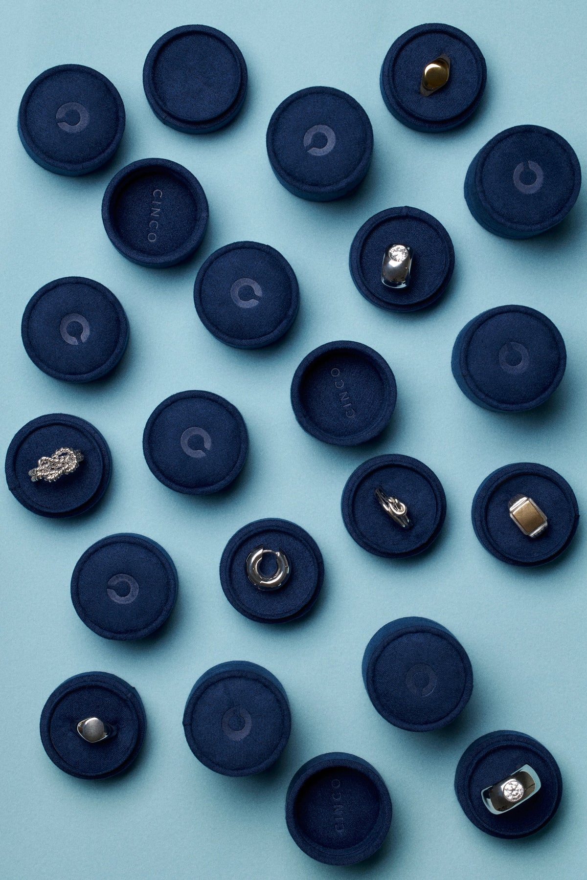 Arrangement of tiny velvet jewelry boxes with various jewelry pieces on a soft blue background.